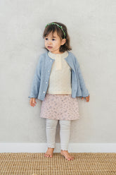 Toddler girl wearing Avauma flower skirt leggings in cream pink with blue cardigan, standing indoors